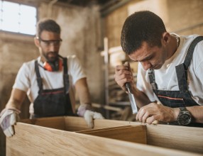 Zwei Schreiner arbeiten mit Werkzeugen an der Erstellung einer Kommode – Symbolbild für eine Gruppenunfallversicherung