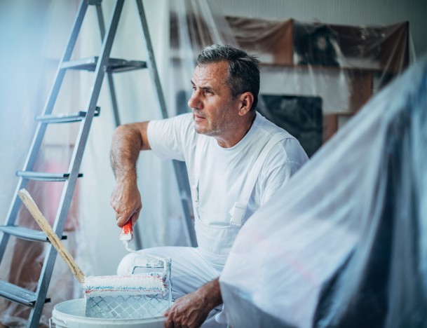 Maler mit Farbroller und Farbeimer bei der Arbeit im Hintergrund eine Leiter
