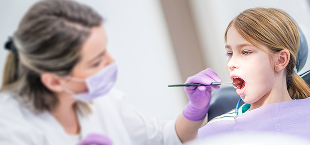 Zahnärztin untersucht ein Mädchen mit einem Mundspiegel – Symbol Bild für eine Krankenzusatzversicherung