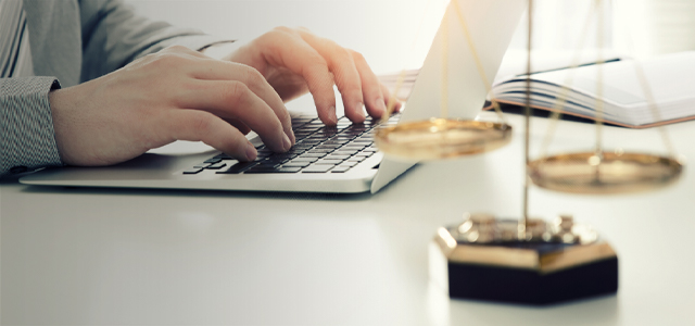 Person tippt auf Laptop, im Vordergrund eine goldene Justitia-Waage – Symbolbild für eine Rechtsschutzversicherung