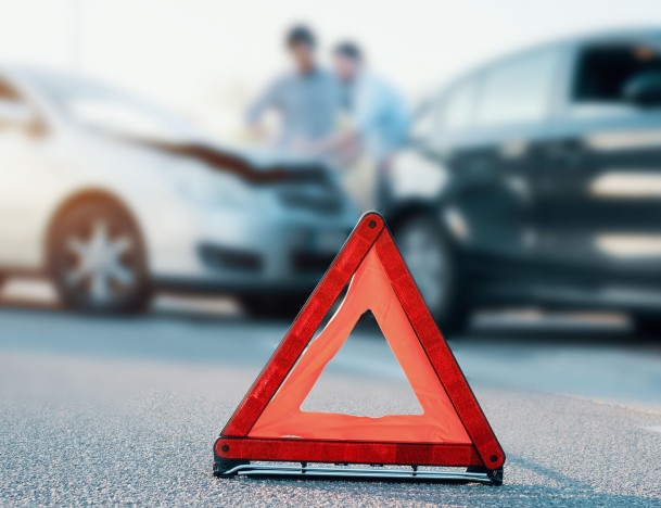 Warndreieck steht vor zwei Autos, die einen Unfall hatten